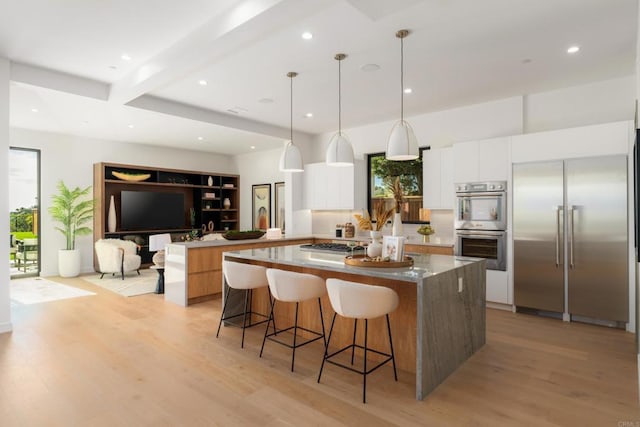 kitchen with a center island, light wood-type flooring, pendant lighting, stainless steel appliances, and white cabinets