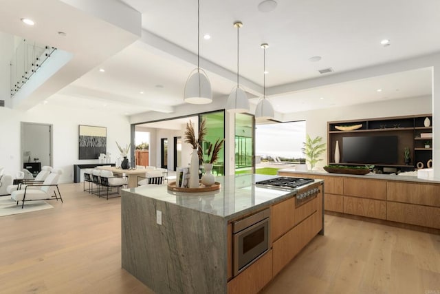 kitchen with stainless steel appliances, hanging light fixtures, a large island, and light hardwood / wood-style flooring