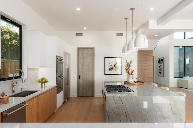 kitchen featuring decorative light fixtures, sink, white cabinets, light stone counters, and stainless steel appliances