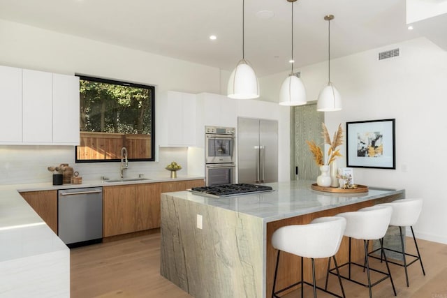 kitchen featuring pendant lighting, sink, stainless steel appliances, a center island, and white cabinets