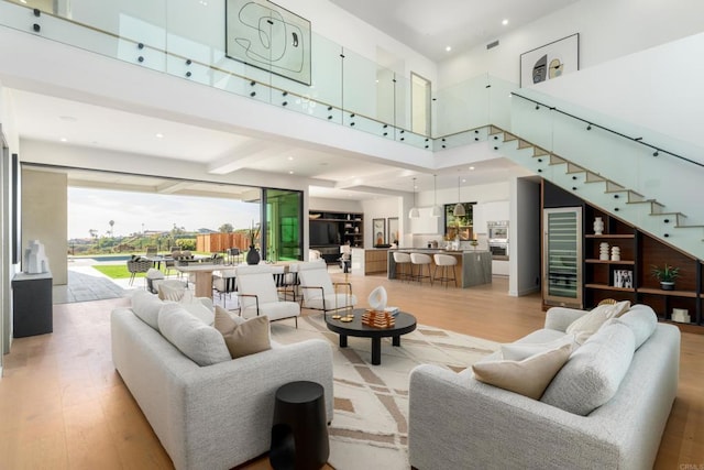 living room featuring a towering ceiling, wine cooler, and light wood-type flooring