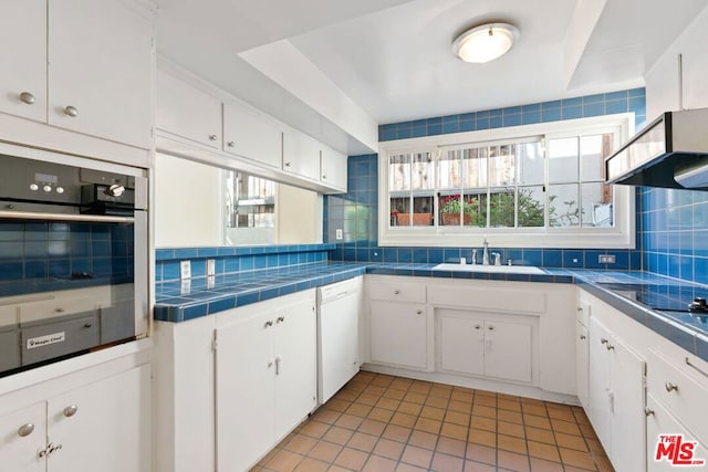 kitchen with tile counters, backsplash, stainless steel oven, and white cabinetry