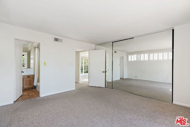 unfurnished bedroom with light colored carpet, ensuite bathroom, and a closet