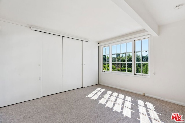 unfurnished bedroom featuring light colored carpet, a closet, and beam ceiling