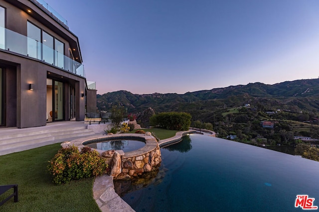 pool at dusk featuring a mountain view, an in ground hot tub, and a patio