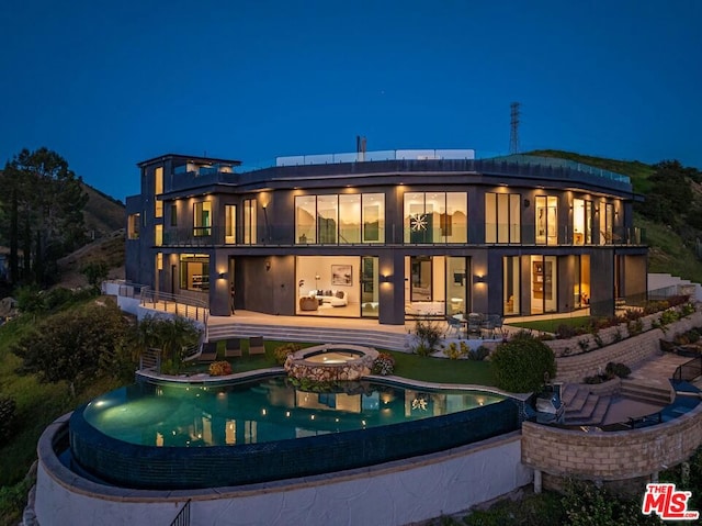 back house at twilight featuring an in ground hot tub and a patio