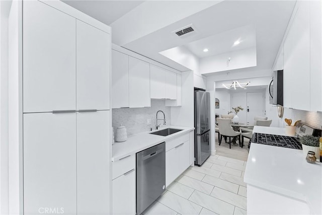 kitchen featuring white cabinets, stainless steel appliances, sink, backsplash, and a raised ceiling