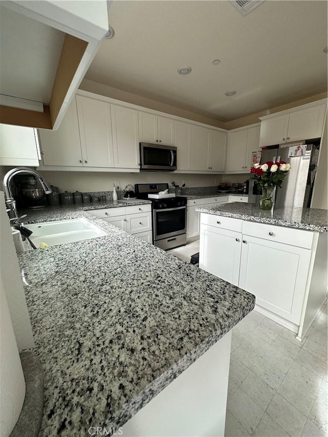 kitchen featuring stainless steel appliances, sink, light stone countertops, white cabinets, and a center island