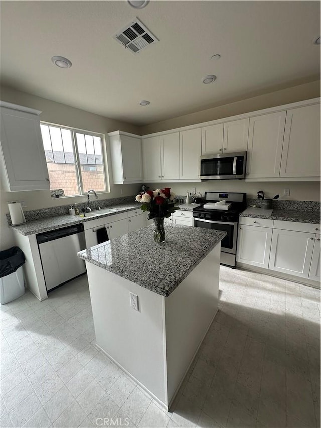 kitchen with light stone countertops, white cabinets, a center island, stainless steel appliances, and sink