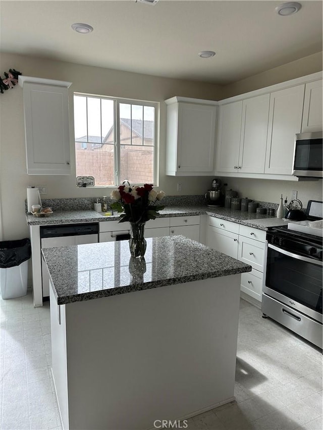 kitchen with light stone countertops, a kitchen island, stainless steel appliances, and white cabinetry