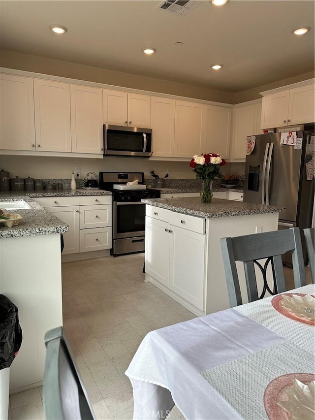 kitchen with appliances with stainless steel finishes, dark stone countertops, white cabinetry, and a center island