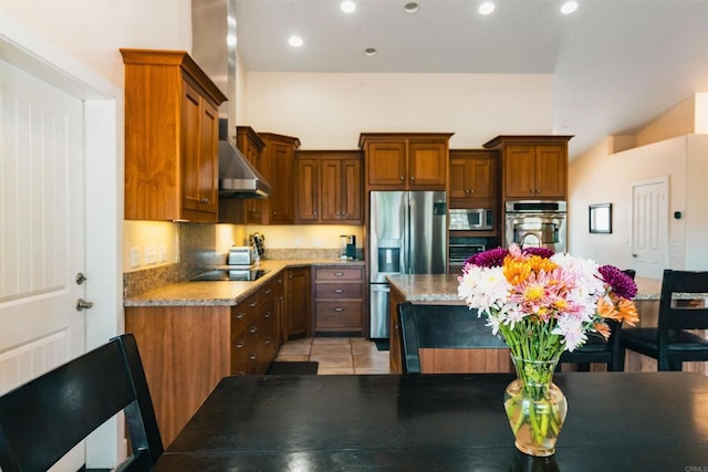 kitchen featuring stainless steel appliances, wall chimney range hood, light stone counters, and light tile patterned floors