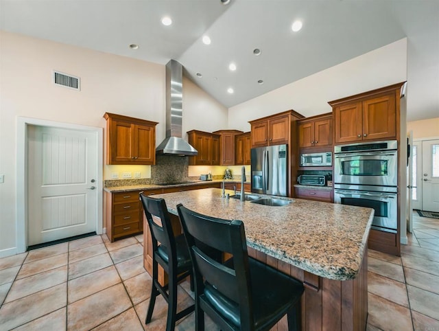 kitchen with stainless steel appliances, a center island with sink, a kitchen bar, and wall chimney exhaust hood