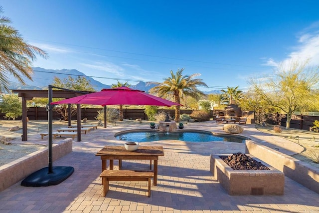 view of pool featuring an outdoor stone fireplace, a patio area, an outdoor fire pit, a mountain view, and pool water feature