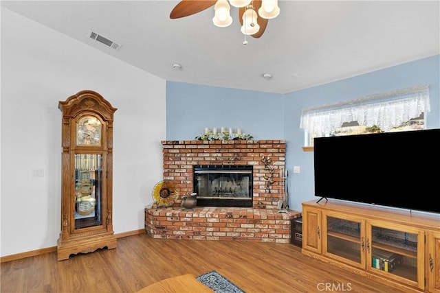 unfurnished living room featuring a brick fireplace, wood finished floors, visible vents, and baseboards