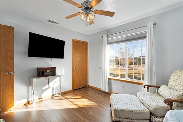 sitting room with visible vents, ceiling fan, baseboards, and wood finished floors