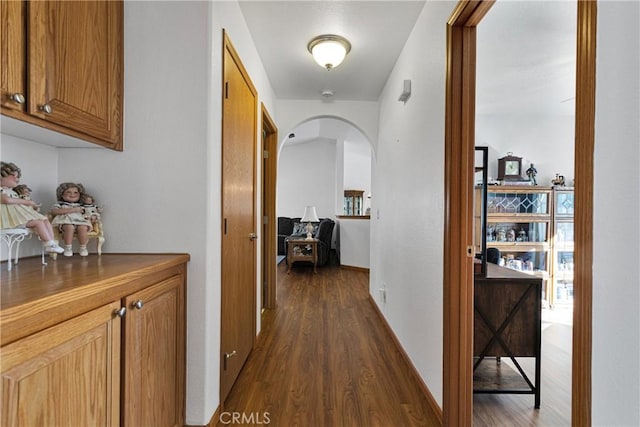 hallway featuring arched walkways, dark wood-type flooring, and baseboards