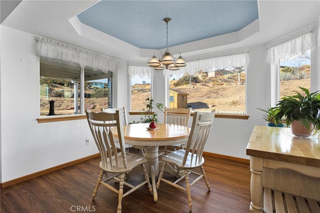 dining space featuring dark wood-style flooring, a notable chandelier, a raised ceiling, a textured ceiling, and baseboards