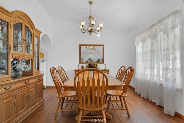 dining area with arched walkways, baseboards, dark wood-style floors, and a chandelier