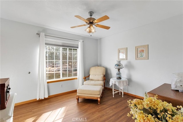 living area featuring a ceiling fan, baseboards, and wood finished floors