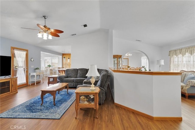 living room with ceiling fan with notable chandelier, wood finished floors, visible vents, baseboards, and vaulted ceiling