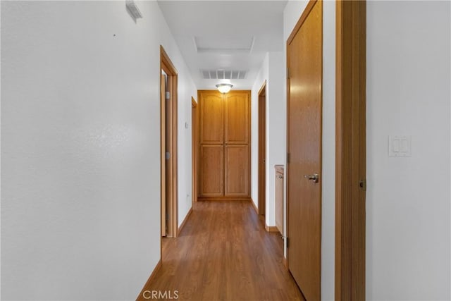 hallway with baseboards, wood finished floors, visible vents, and attic access