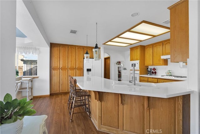 kitchen with arched walkways, a peninsula, white appliances, brown cabinets, and dark wood finished floors