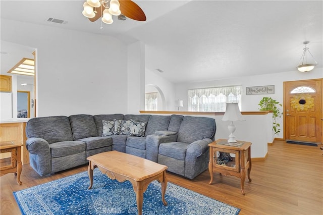 living area featuring lofted ceiling, a ceiling fan, visible vents, and light wood-style floors