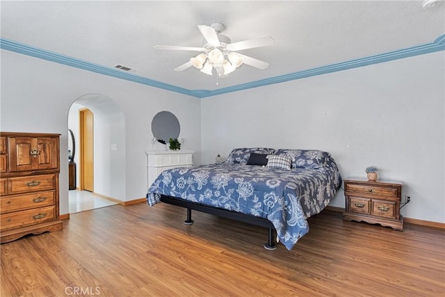 bedroom featuring arched walkways, visible vents, baseboards, ornamental molding, and light wood finished floors