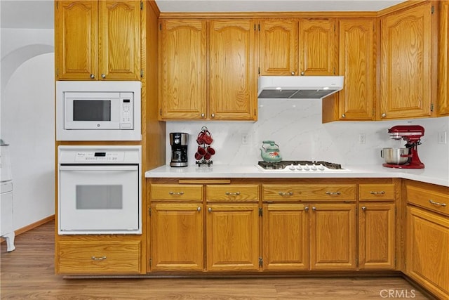 kitchen with arched walkways, light countertops, white appliances, and under cabinet range hood