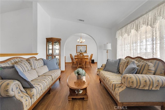 living room with arched walkways, lofted ceiling, a notable chandelier, wood finished floors, and visible vents