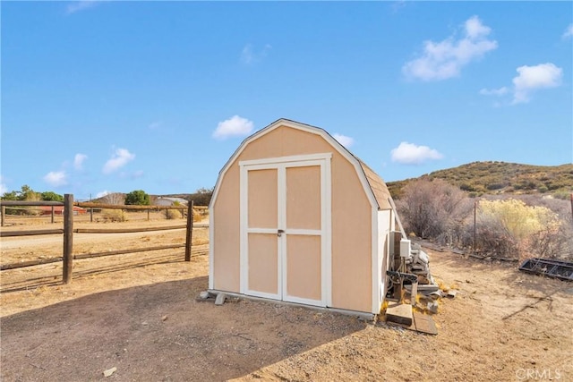 view of shed with fence, a mountain view, and a rural view