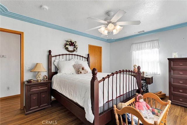 bedroom featuring a textured ceiling, wood finished floors, a ceiling fan, visible vents, and crown molding