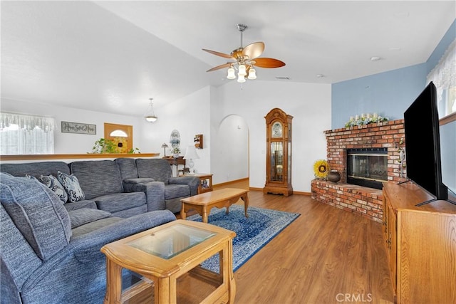 living area featuring wood finished floors, visible vents, baseboards, vaulted ceiling, and a brick fireplace