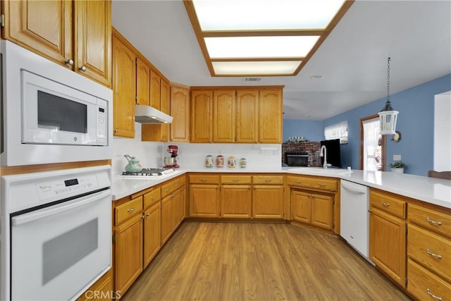 kitchen with under cabinet range hood, white appliances, a sink, light countertops, and light wood-type flooring