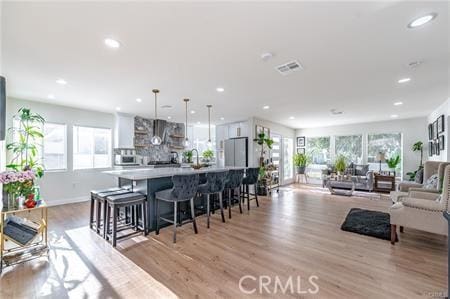 kitchen with a kitchen breakfast bar, white cabinetry, pendant lighting, and light hardwood / wood-style flooring