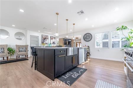 kitchen with a kitchen bar, pendant lighting, light hardwood / wood-style floors, and a kitchen island with sink