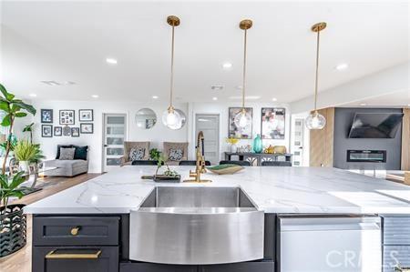 kitchen with light stone countertops, decorative light fixtures, a center island with sink, and sink