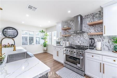 kitchen featuring tasteful backsplash, wall chimney range hood, light stone countertops, appliances with stainless steel finishes, and white cabinets