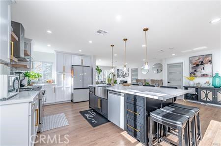 kitchen featuring a spacious island, white appliances, white cabinets, hanging light fixtures, and a breakfast bar area