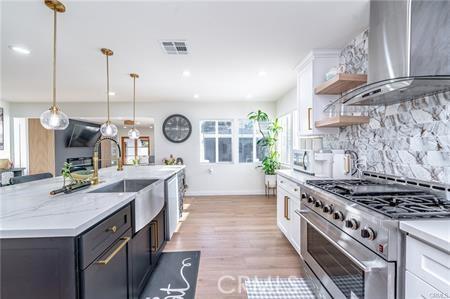 kitchen with pendant lighting, white cabinets, appliances with stainless steel finishes, wall chimney exhaust hood, and a center island with sink