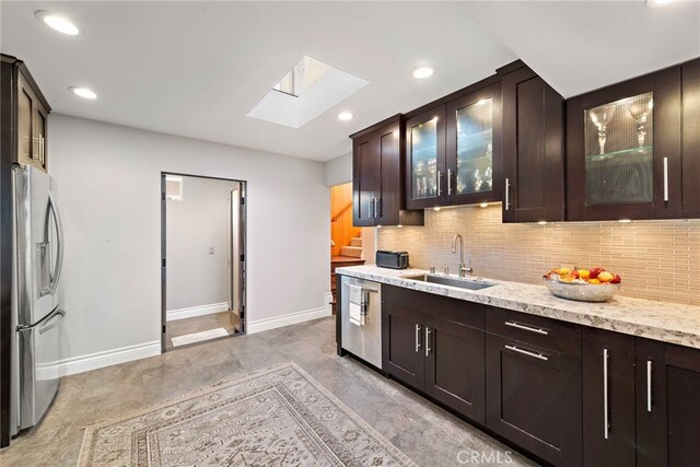 kitchen featuring appliances with stainless steel finishes, sink, light stone countertops, a skylight, and dark brown cabinetry