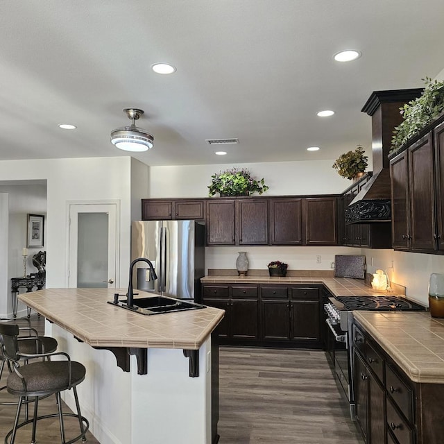 kitchen featuring tile counters, ventilation hood, stainless steel appliances, and dark brown cabinetry