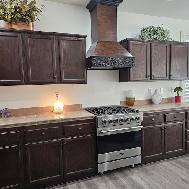 kitchen featuring custom exhaust hood, tile countertops, dark brown cabinets, and high end range