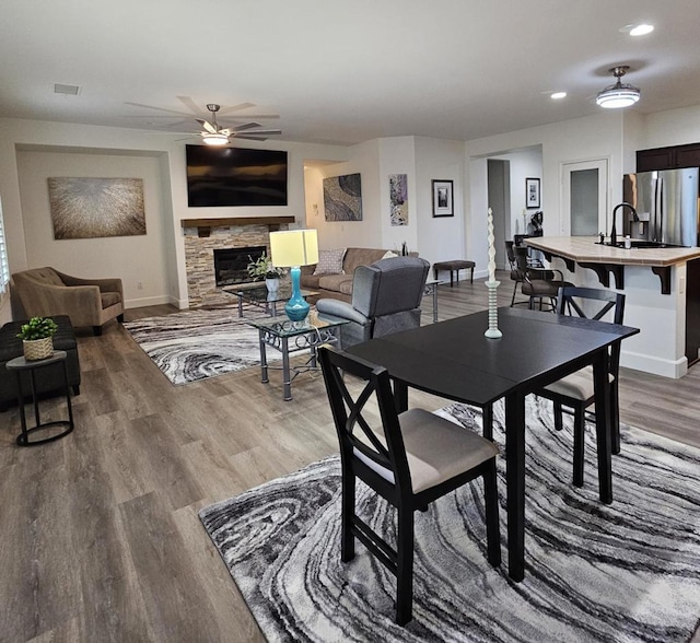 dining space featuring ceiling fan, wood-type flooring, a stone fireplace, and sink