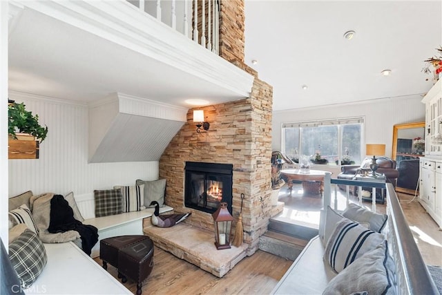 living room with light hardwood / wood-style flooring, ornamental molding, and a stone fireplace