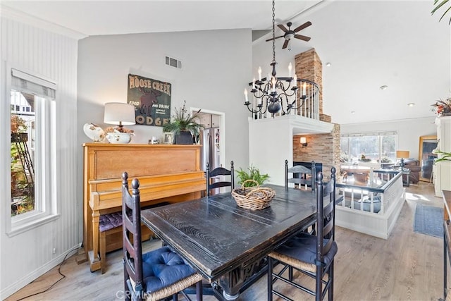 dining space with vaulted ceiling, ceiling fan with notable chandelier, and light hardwood / wood-style floors