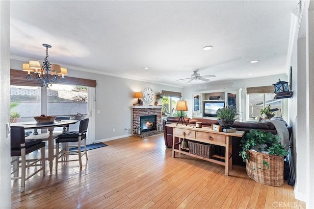 living room featuring a fireplace, plenty of natural light, ceiling fan with notable chandelier, and crown molding