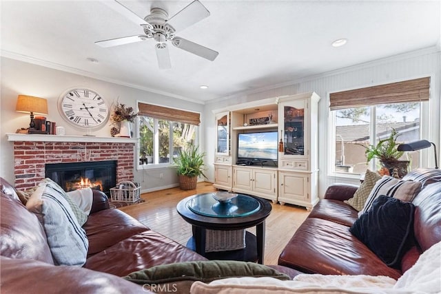 living room with a brick fireplace, ornamental molding, ceiling fan, and light wood-type flooring