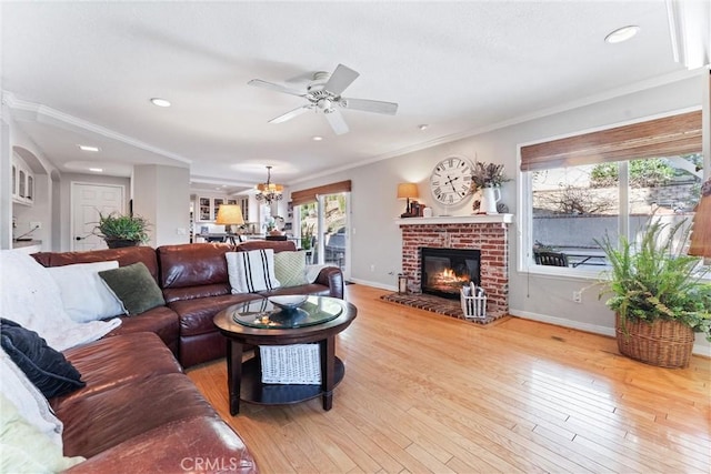 living room featuring a brick fireplace, ceiling fan with notable chandelier, ornamental molding, and light wood-type flooring